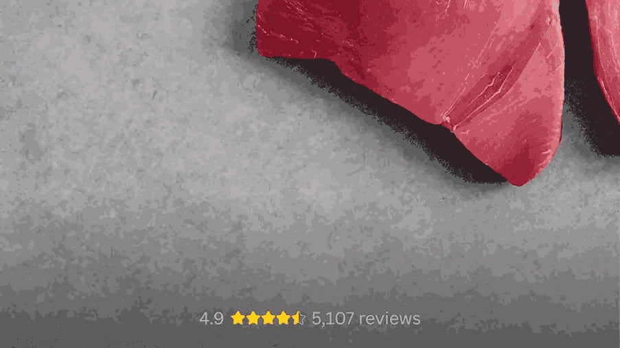 Close-up of two fresh red tuna fillets on a textured grey surface.