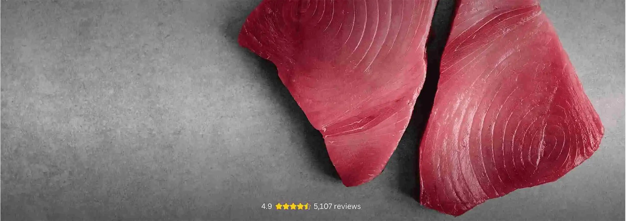 Close-up of two fresh red tuna fillets on a textured grey surface.